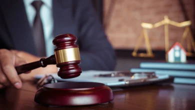 Person im Anzug hält einen Richterhammer, im Hintergrund Justizwaage und Hausmodell.