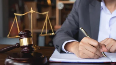 Eine Person im Anzug schreibt auf ein Dokument an einem Schreibtisch mit Richterhammer und Justizwaage.