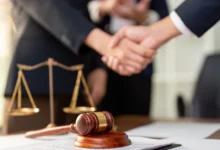 Händeschütteln über einem Schreibtisch mit Richterhammer und Justizwaage.